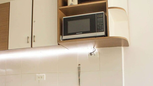 Een keuken met een magnetron, witte kastjes, een houten plank en een eethoek met een tafel gedekt voor twee personen.