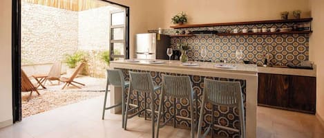 Una cocina con barra, pared de piedra y vista a un espacio exterior con mesas.