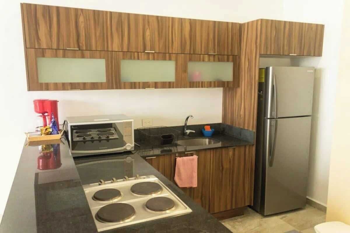 A modern kitchen with wooden cabinets, a stainless steel refrigerator, a gas stove, and a black countertop.