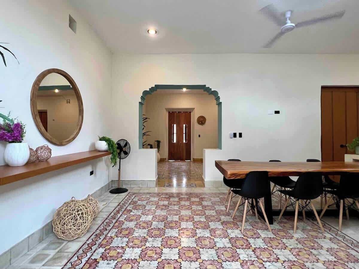 A dining area with a wooden table and chairs, a mirror, and a decorative rug.