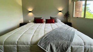 Un dormitorio con una cama grande, dos mesitas de noche y una ventana con vistas a zonas verdes.