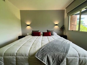 Ein Schlafzimmer mit einem großen Bett, zwei Nachttischen und einem Fenster mit Blick auf Grünflächen.