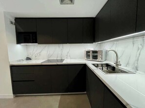 Une cuisine moderne avec des meubles noirs, un plan de travail blanc, un four à micro-ondes encastré et un évier en acier inoxydable.