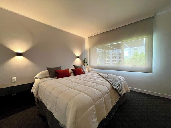 A modern bedroom with a large bed, two wall-mounted lights, a window with a view, and a dark carpet. - PH Altamira: Terraza Panorámica (Caracas)