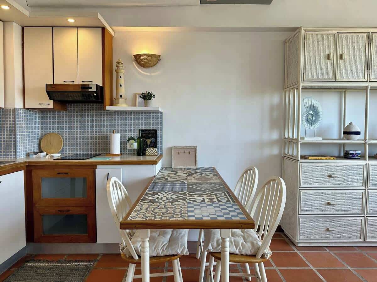 Una cocina compacta con salpicadero de azulejos, encimera de madera y una mesa con sillas.