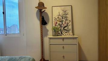 Una habitación con cama, cómoda con cajones, lámpara de pie e imagen colgada en la pared.