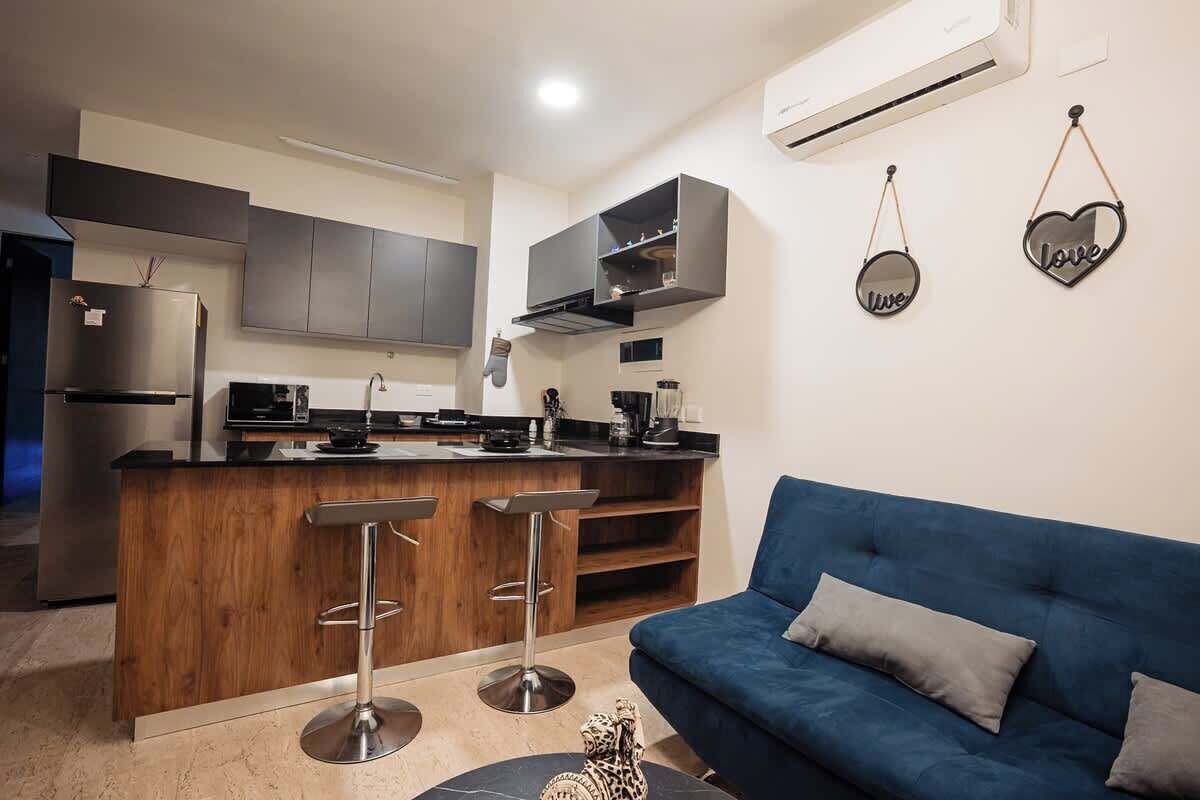 Uma cozinha moderna com uma ilha central, banquetas e um sofá azul numa sala de estar.