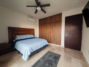 A bedroom with a bed, a ceiling fan, a wardrobe, and a door.