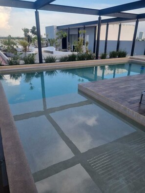 A swimming pool with clear water, surrounded by a wooden deck and potted plants.