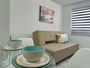 Una sala de estar moderna con un sofá, una mesa de comedor con cuencos y vasos, y un cuadro en la pared.
