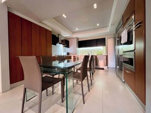 A modern kitchen with a glass dining table and chairs, stainless steel appliances, and wooden cabinets. - Lux+comfort at Campo Alegre|Design & connectivity (Caracas)