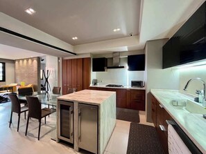 A modern kitchen with a central island, built-in appliances, and a dining area with a glass table. - Lux+comfort at Campo Alegre|Design & connectivity (Caracas)