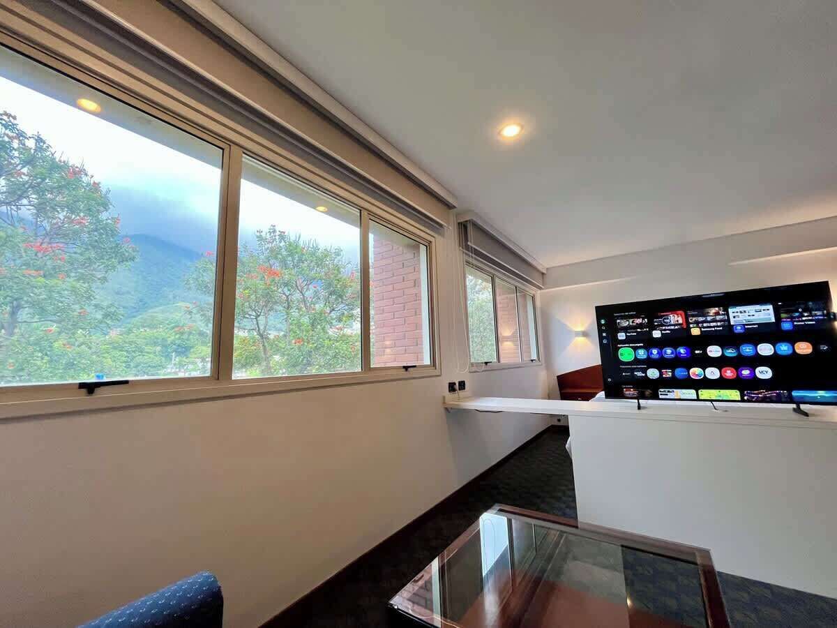 Una habitación con un ventanal grande, un televisor de pantalla plana y una mesa de vidrio.