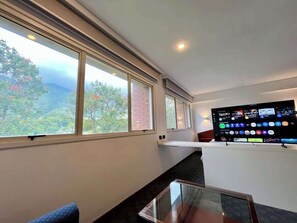 Una habitación con un ventanal grande, un televisor de pantalla plana y una mesa de vidrio.