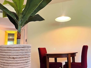 A dining area with a table and chairs, a potted plant, and a ceiling light fixture.