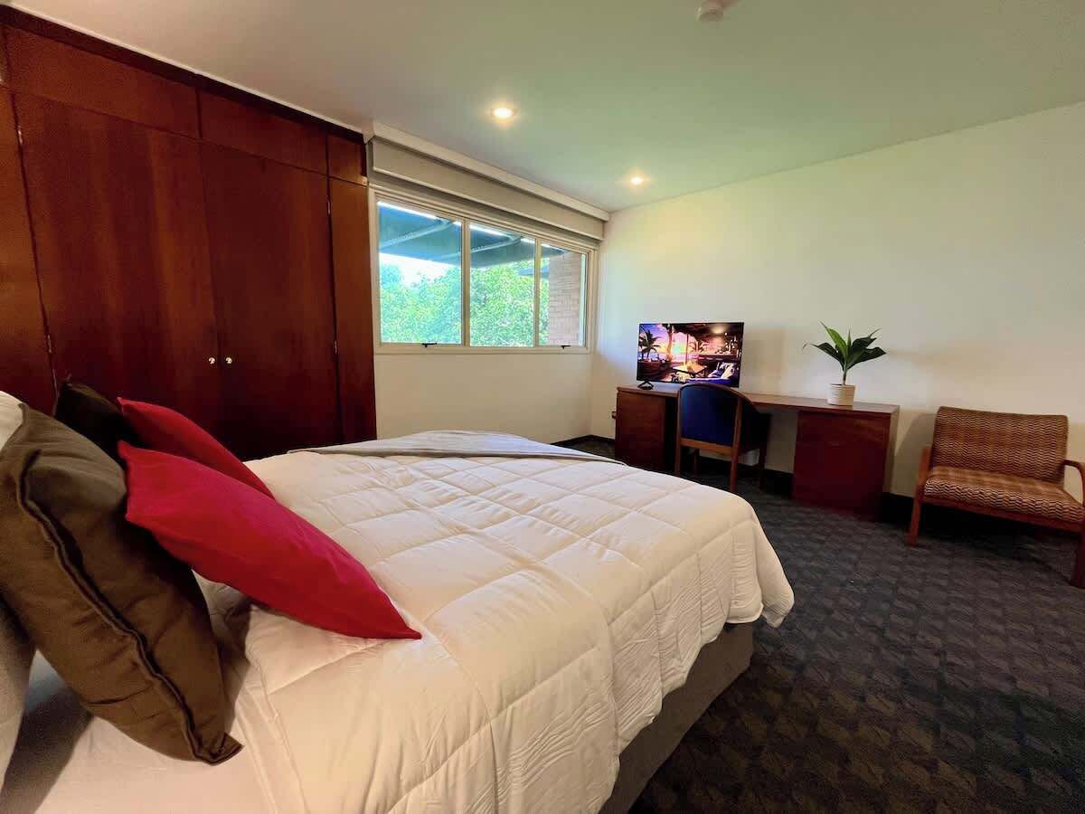 A bedroom with a bed, a desk, a chair, and a window.