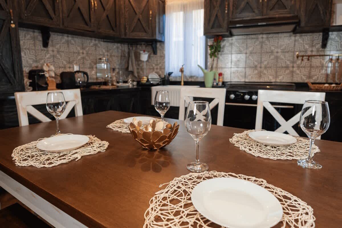 A dining table set with white plates and wine glasses, surrounded by chairs.