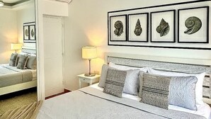 Um quarto com uma cama, mesas de cabeceira, um espelho e quadros nas paredes.