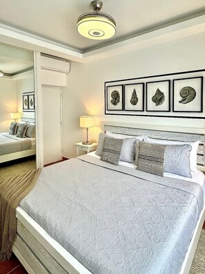 Ein Schlafzimmer mit Bett, Nachttischen, einem Spiegel und gerahmten Kunstwerken an der Wand.