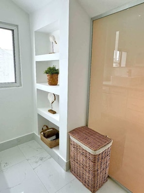 A corner of a room with a white tiled floor, a white wall, a white door, and a white shelf with a plant and a decorative item. - Apartment w/ balcony + Pool | Playa Bibijagua (Punta Cana)