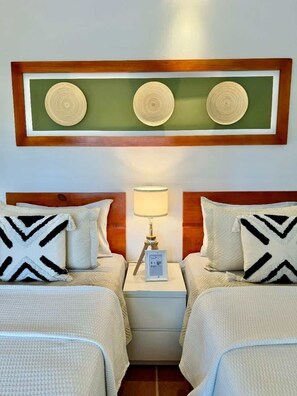 A hotel room with two beds, a nightstand with a lamp, and a wall-mounted decorative piece above the beds. - Apartment w/ balcony + Pool | Playa Bibijagua (Punta Cana)