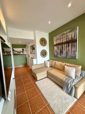 A living room with a beige sectional sofa, a white rug, and a green accent wall. - Apartment w/ balcony + Pool | Playa Bibijagua (Punta Cana)