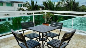 Terraço com mesa e cadeiras, vista para uma piscina e palmeiras.