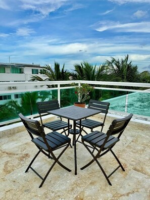 Eine Terrasse mit Tisch und Stühlen, mit Blick auf ein Schwimmbecken und Palmen.
