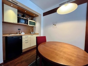 Eine kleine Küche mit einer Mikrowelle, einem kleinen Kühlschrank und einem Holzespeise Tisch mit einem roten Stuhl.
