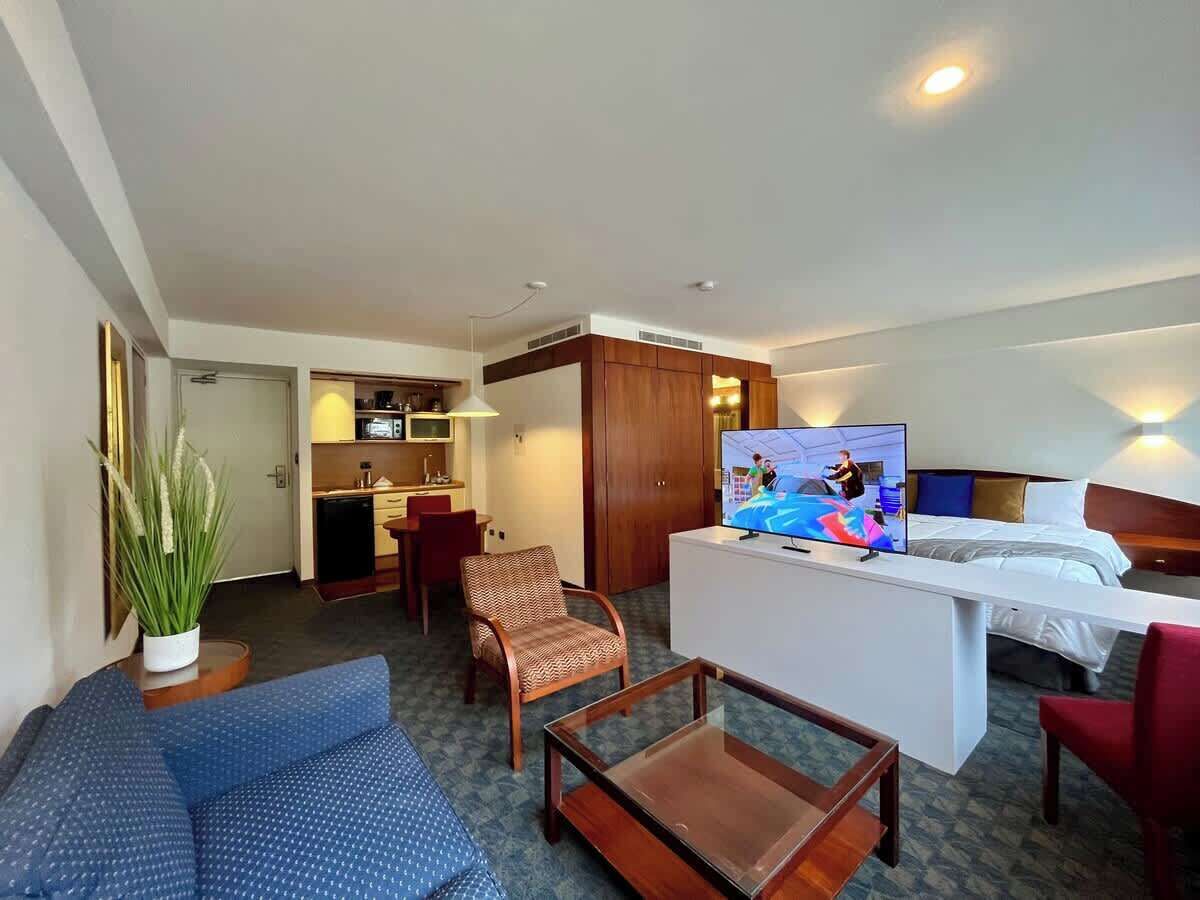 A hotel room with a bed, a TV, a sofa, a desk, and a kitchenette.