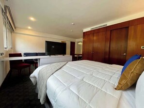 Ein Hotelzimmer mit einem großen Bett, einem Schreibtisch mit Stuhl, einem Fernseher und einem Kleiderschrank.