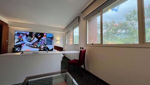 A hotel room with a large flat-screen TV, a small table, a red chair, and a window with a view of trees. - Tu escape en caracas, apartamento moderno (Caracas)