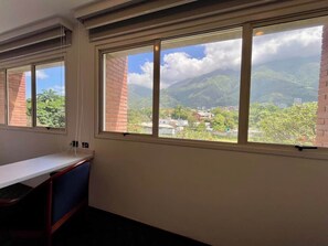 Ein Zimmer mit Schreibtisch und einem großen Fenster mit Blick auf eine gebirgige Landschaft.