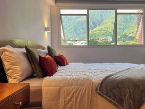 A bedroom with a bed, pillows, a nightstand, and a window with a view of a mountainous landscape. - Tu Rincón en Altamira: ¡Céntrico y Nuevo! (Caracas)