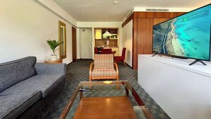 Hotellihuone, jossa on sohva, pieni pöytä, televisio, ruokailutila ja kasvi.