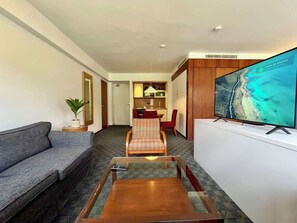 Ein Hotelzimmer mit Sofa, kleinem Tisch, Fernseher, Essbereich und einer Pflanze.