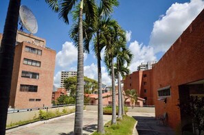A courtyard with palm trees, brick buildings, and a satellite dish. - Tu Rincón en Altamira: ¡Céntrico y Nuevo! (Caracas)