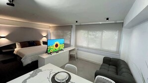 A modern hotel room with a bed, a desk with a TV, a dining table, and a sofa. - Disfruta de esta acogedora habitación en Caracas (Caracas)