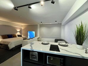 Ein modernes Hotelzimmer mit einem Bett, einem Schreibtisch mit Computer, einem Fernseher und einer Pflanze.