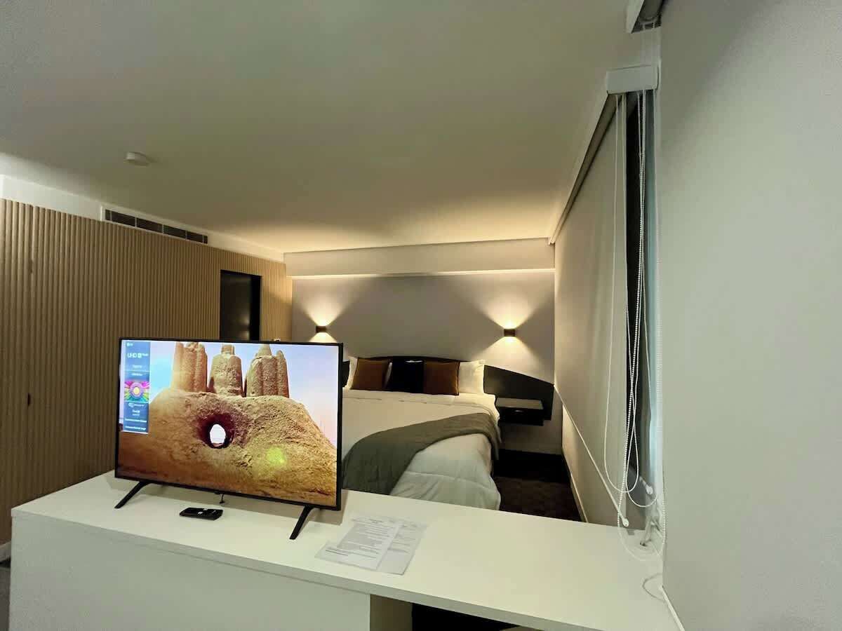 Ein Hotelzimmer mit Bett, Nachttisch, Fernseher und einem fenster mit Vorhängen.
