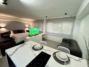 A modern hotel room with a bed, a dining area with a marble table, and a large window with blinds. - Disfruta de esta acogedora habitación en Caracas (Caracas)