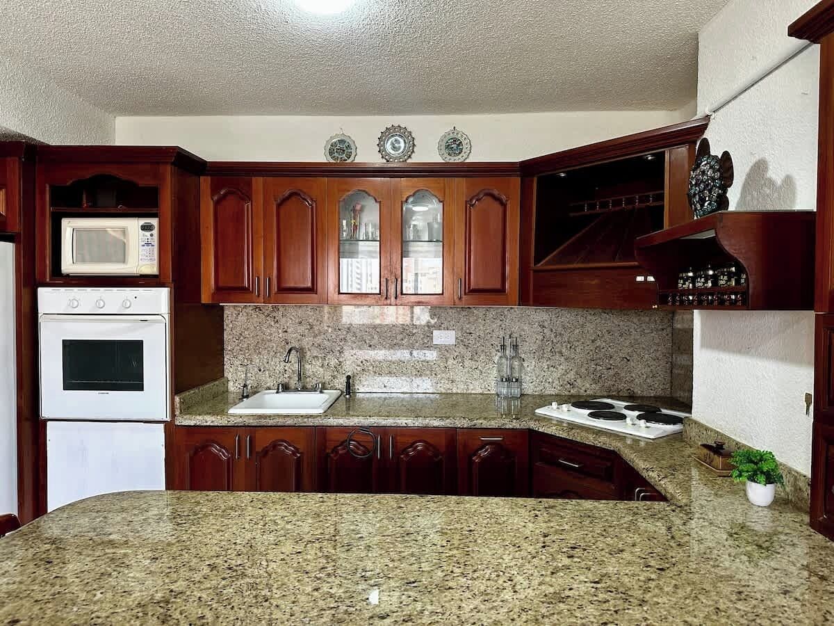 Eine Küche mit Granit Arbeitsplatten, Holzschränken, einer Mikrowelle, einem Backofen und einem Spülbecken.