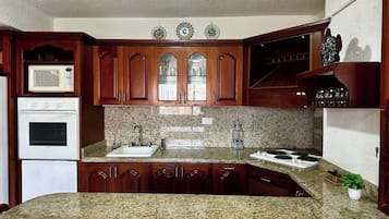 Eine Küche mit Granit Arbeitsplatten, Holzschränken, einer Mikrowelle, einem Backofen und einem Spülbecken.