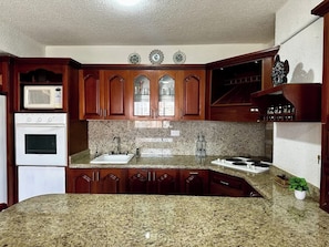A kitchen with granite countertops, wooden cabinets, a microwave, an oven, and a sink.