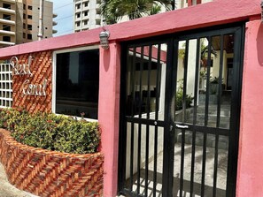 Un edificio de fachada roja y una puerta negra, con un muro de ladrillo y una ventana.