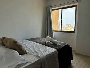Una stanza con un letto, un tavolino, una finestra con tende e vista sugli edifici.