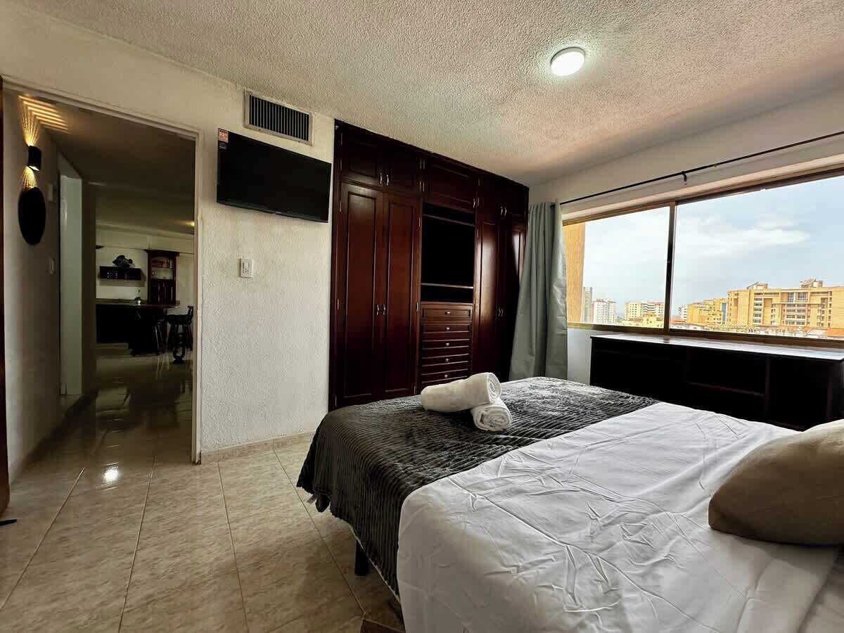 Een hotelkamer met een bed, een kledingkast, een televisie en uitzicht op de stad.