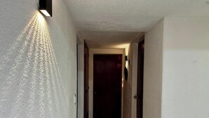 Un couloir étroit, avec un luminaire sur le côté gauche et une porte au fond.