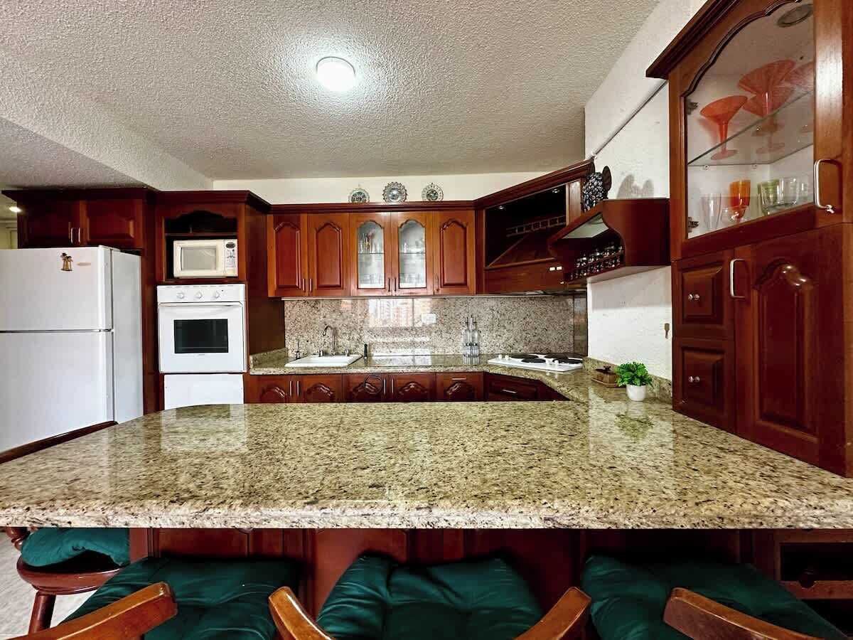A kitchen with granite countertops, wooden cabinets, a microwave, an oven, and a sink.