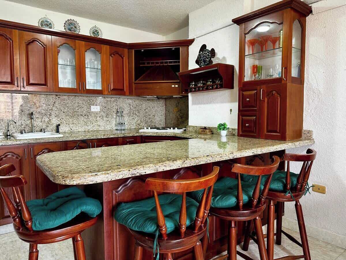 A kitchen with granite countertops, wooden cabinets, and bar stools with cushioned seats.